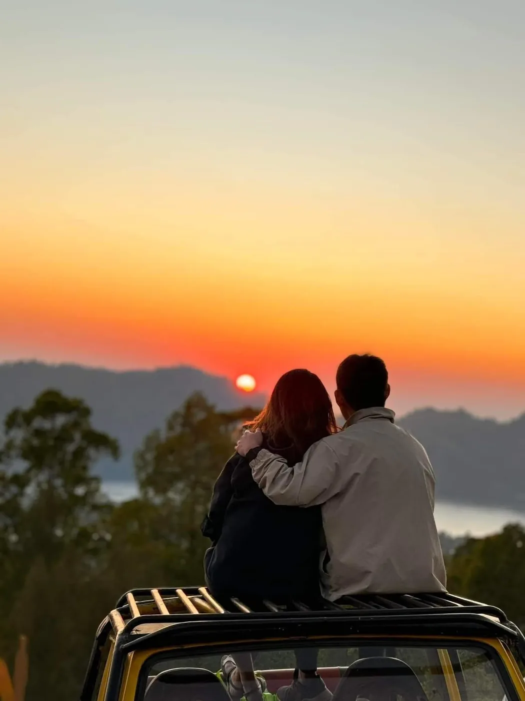Two guests watching sunrise from the roof of the jeep